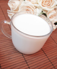 Cup of fresh with milk and creamy roses on wooden background
