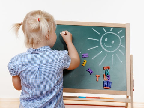 Blond Child writing the ABC on a blackboard