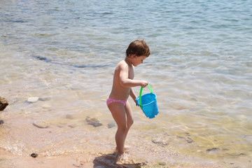 Four years old girl with the blue bucket on the sea