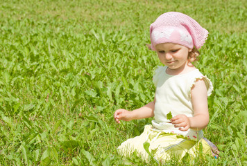 A little girl sits on a green lawn