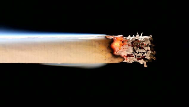 Macro view of burning cigarette with smoke on black