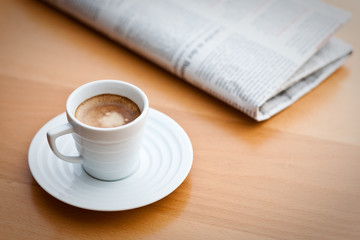 Espresso in weißer Tasse, mit Tageszeitung auf Holztisch