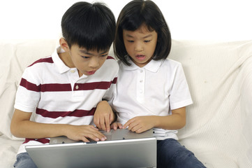 Boy and girl using a laptop at home on sofa