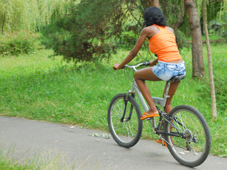 Fototapeta na wymiar african girl having fun riding a bike in park