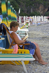 A woman at beach reading a book on a deckchair