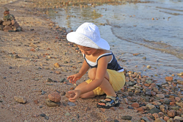 little girl puts stones on the beach - obrazy, fototapety, plakaty