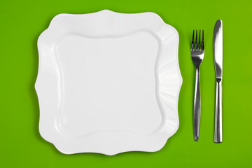 Knife, figured white plate and fork on green background