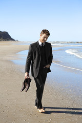 Young businessman walking on beach  barefoot and holding shoes