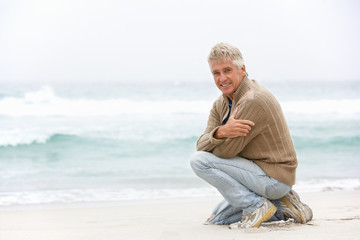 Fototapeta na wymiar Senior Man On Holiday Kneeling On Winter Beach
