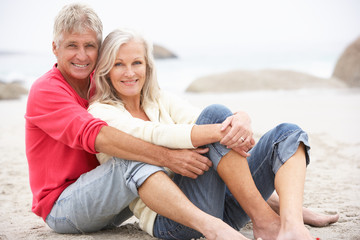 Senior Couple On Holiday Sitting On Winter Beach