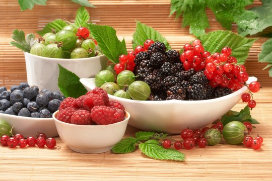Berries in plates, on a table, among green leaves