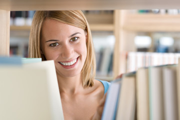 Student in library - cheerful woman look through bookshelf