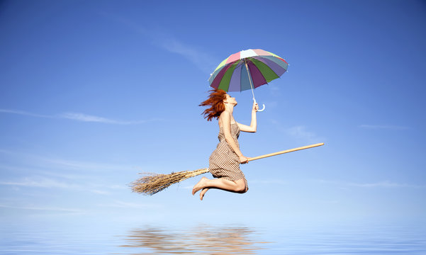 Young red-haired witch on broom flying with umbrella over water