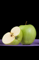 Fresh green apples on the purple plate and black background