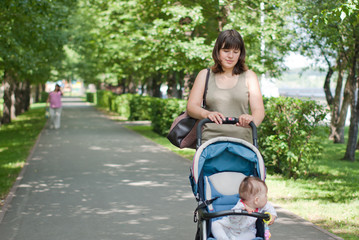a young mother walking with a baby carriage in the park