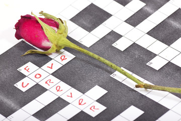 Dry pink red rose on a crossword paper with love text