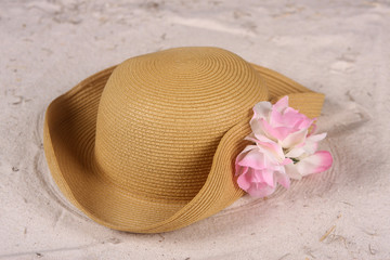Fototapeta na wymiar Woman's beach hat laying in the sand with pink orchid