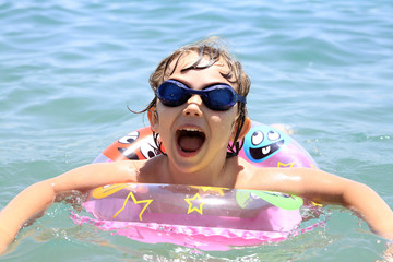 a little girl with glasses swims in the sea - obrazy, fototapety, plakaty