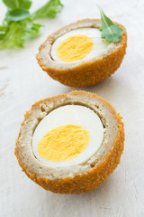 Scotch egg on a white board with green salad