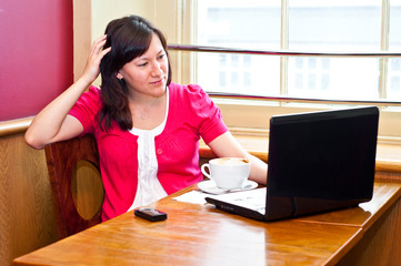 young woman drinking cappuccino using her laptop in a cafe