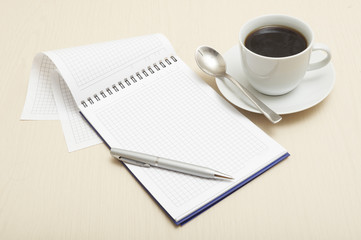Coffee cup and spiral notebook and pen on the wooden table