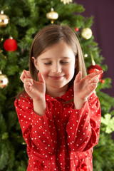 Young Girl Crossing Fingers In Front Of Christmas Tree