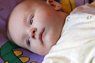 Serious baby is lying on the bed