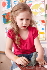 Child girl mould from clay in play room.