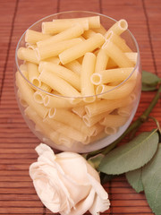 Food theme: uncooked pasta and creamy rose on wooden background