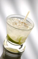 Glass of caipirinha with straw in front of a light background
