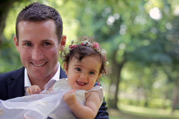 Fröhliches Baby Mädchen in weißem Kleid auf Arm von Vater. Feier wie Taufe oder Hochzeit.