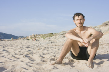 Fototapeta na wymiar Young man sitting in the sand of a beach - Sardinia, Italy