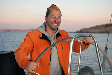 young man holding the steering wheel on the yacht