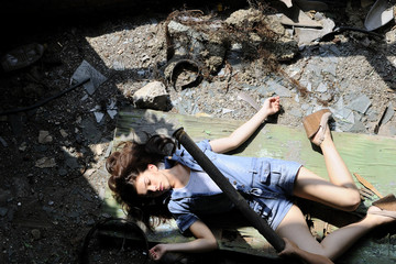 slim young woman simulating suicide in devastated place