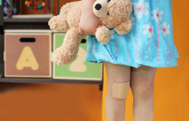 a girl holding a teddy with a big plaster on her knee