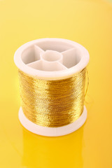 bobbin with golden thread on yellow background