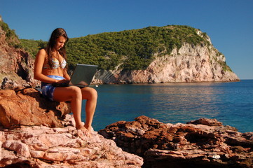 Dziewczyna z laptopem na skalistej plaży - obrazy, fototapety, plakaty