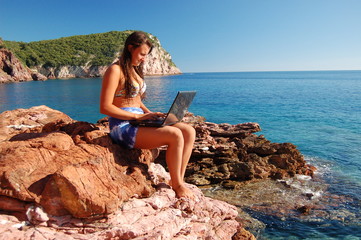 Fototapeta na wymiar Dziewczyna z laptopem na skalistej plaży