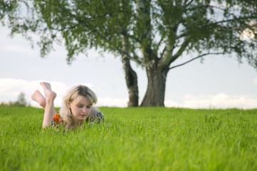 Fototapeta premium Young beautiful woman lays on green field and reads