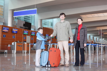 family with boy standing in airport hall with suitcases full bod