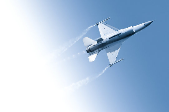 military fighter jet flying through a gradient blue sky