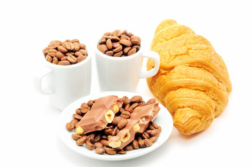 two cups and plate filled with coffee beans and croissant