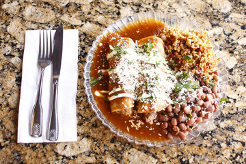 A plate of gourmet enchiladas with rice and beans.