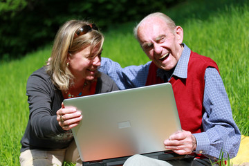 Alter Mann und junge Frau lachend am Laptop im Grünen