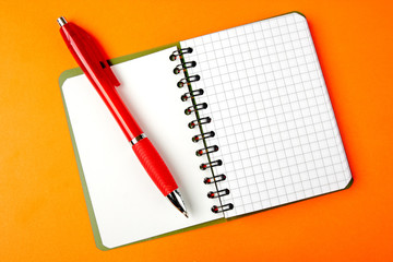Opened notebook squared pagewith red pen over it on orange backg