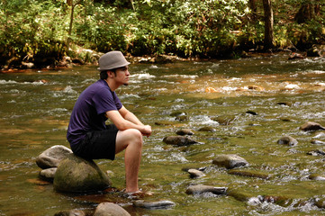 Teen sitting on river rocks, side view