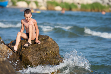 Little boy sitting on rocks at sea