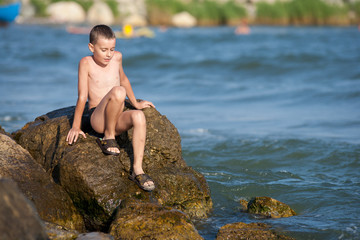 Fototapeta premium Little boy sitting on rocks at sea