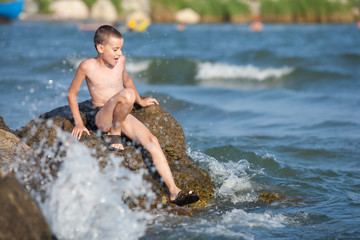 Little boy sitting on rocks at sea