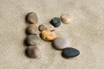 Fototapeta na wymiar lettre K en galets zen dans le sable